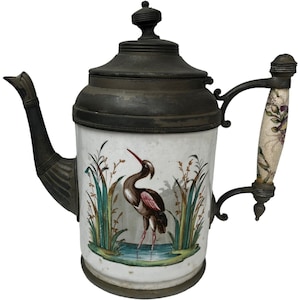 Könnte beinhalten: Eine weiße Teekanne aus Keramik mit einem schwarzen Metalldeckel und -griff. Die Teekanne hat ein bemaltes Design eines Vogels, der in einem Teich mit Schilf steht.