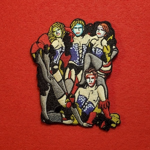 May include: Embroidered patch depicting five figures in colourful costumes and masks. The figures are grouped together, some standing and others seated. The patch has a whimsical and theatrical feel.