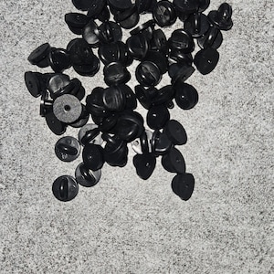 May include: A pile of black plastic pin back closures for badges or buttons.