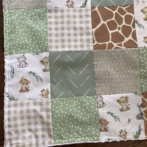 May include: A patchwork baby blanket featuring squares of various patterns and colors. The design includes squares with safari animal illustrations, polka dots, gingham, and giraffe print. The color palette consists of green, tan, and white.