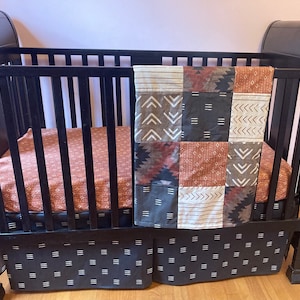 May include: A black crib with a brown and white patterned crib sheet and a brown, white, and black patchwork quilt. The crib has a black and white patterned skirt.