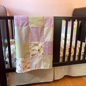 Op de afbeelding: Een donkerbruin ledikant met een patchwork quilt en bijpassende bedrok. De quilt heeft vierkanten met lavendel-, groene en bloempatronen. De bedrok en sommige quiltvierkanten hebben een groen-wit ruitpatroon.