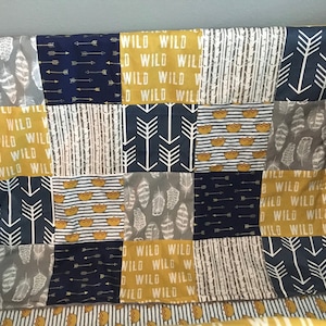May include: A patchwork baby blanket with a variety of patterns, including arrows, feathers, and crowns. The blanket is made in shades of gray, blue, and yellow.