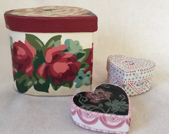 May include: Three heart-shaped boxes with floral patterns. The largest box is white with red and pink roses, the medium box is white with blue and red polka dots, and the smallest box is black with pink and green flowers.