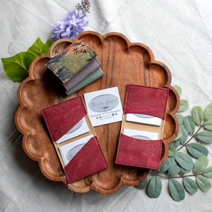 May include: A wooden tray holds several cork business card holders in burgundy and green. The card holders are open, displaying white cards. A small card with text that reads "The Lilac Nook" is also visible.