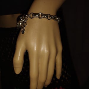 May include: Silver-toned bracelet with a chain-link design. The bracelet features a heart-shaped charm and a decorative charm. The bracelet is worn on a mannequin hand.