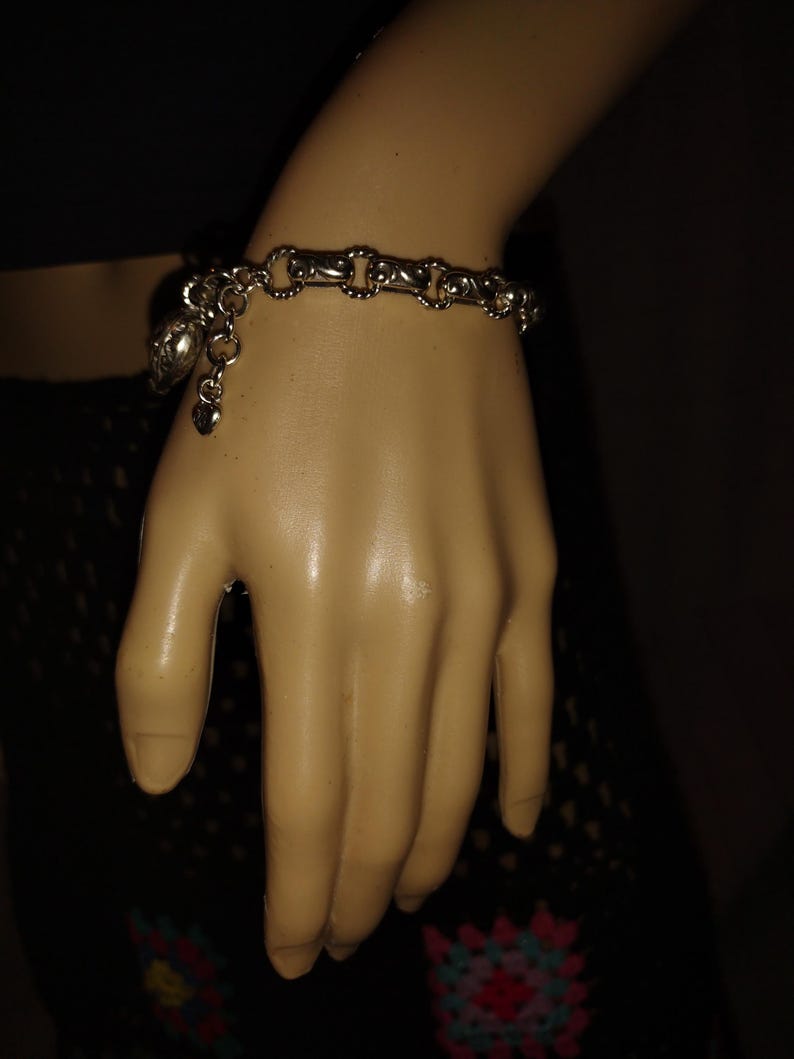 May include: Silver-toned bracelet with a chain-link design. The bracelet features a heart-shaped charm and a decorative charm. The bracelet is worn on a mannequin hand.