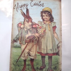 Può includere: Biglietto di Pasqua vintage con un coniglio vestito con un abito che trasporta un cesto di uova, che cammina con una ragazza in un vestito. Il biglietto presenta la scritta "Happy Easter" in corsivo su uno sfondo azzurro.