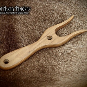 Puede incluir: Una herramienta de madera con un mango largo y dos puntas en el extremo. La herramienta está hecha de madera marrón claro y tiene un acabado liso. Es una herramienta tradicional que se utiliza para hacer hilo.