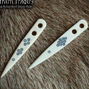 Può includere: Due lesine in osso con cerchi decorativi e fori. Le lesine sono appuntite a un'estremità e hanno un manico arrotondato all'altra estremità.