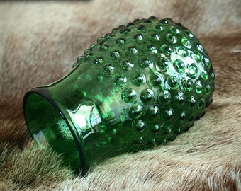 May include: A green glass vase with a textured, bubbled surface. The vase is lying on a brown fur surface.