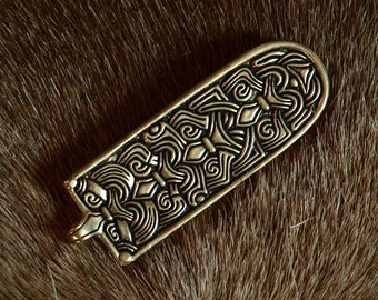 May include: A gold-colored metal pendant with intricate Celtic knotwork designs. The pendant is shaped like a long rectangle with rounded edges.