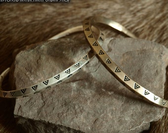 May include: Two gold-toned bracelets with a black triangle pattern. The bracelets are on a gray rock.