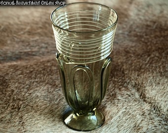 May include: A green glass drinking goblet with a ribbed design and a flared base. The goblet is sitting on a brown fur surface.