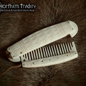 May include: A white bone folding comb with intricate carved designs. The comb is closed and has a leather cord attached to it.