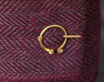 May include: A close-up of a pair of red and gray herringbone patterned pants with a gold metal ring clasp. The pants have a fold-over detail at the bottom. The brand name "BURGSCHNEIDER" is visible on the waistband.