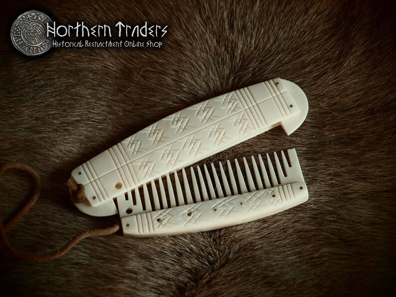 May include: A white bone folding comb with intricate carved designs. The comb is closed and has a leather cord attached to it.