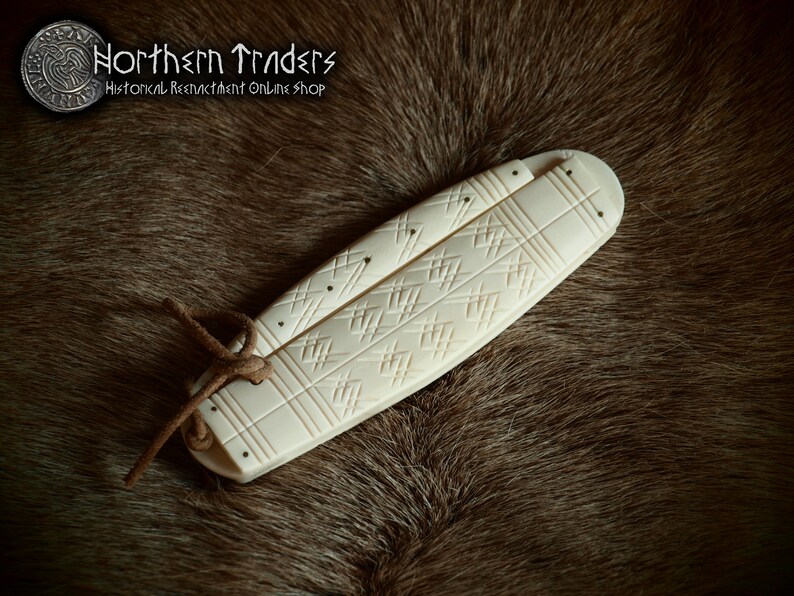 May include: A white bone folding knife with a carved geometric pattern. The knife is closed and tied with a brown leather cord.