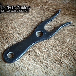 May include: A black two-pronged fork with a smooth, polished finish. The utensil features a circular hole at the base of the handle and a second circular hole positioned between the two prongs. The fork has a curved, elongated design.