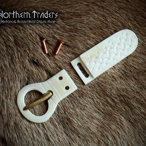 May include: A white bone belt buckle with a brass buckle and two copper rivets. The buckle is in the shape of a circle with a decorative design. The belt strap is also made of white bone and has a woven pattern.