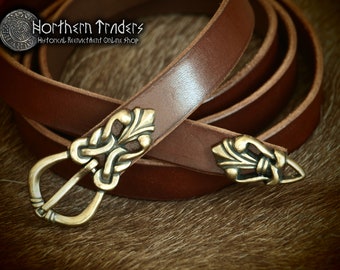May include: A brown leather belt with a brass buckle and two decorative brass accents. The belt is coiled on a brown furry surface.