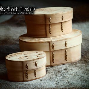 May include: Three wooden oval boxes with lids, stacked on top of each other. The boxes are made of light wood with a natural grain pattern and have decorative brass accents. The boxes are labeled "Northern Traders" and "Historical Reenactment Online Shop".