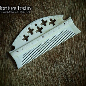 May include: An off-white comb with a decorative top featuring cross-shaped cutouts and small circular accents. The comb's teeth are finely spaced. The image includes the text "Northern Traders Historical Reenactment Online Shop".