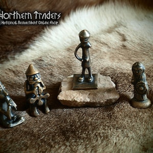 May include: Four small bronze figurines on a brown fur background. The figurines are of a standing person, a person holding a cross, a person with a hat, and a person holding a round object.