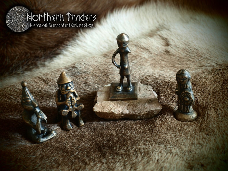 May include: Four small bronze figurines on a brown fur background. The figurines are of a standing person, a person holding a cross, a person with a hat, and a person holding a round object.