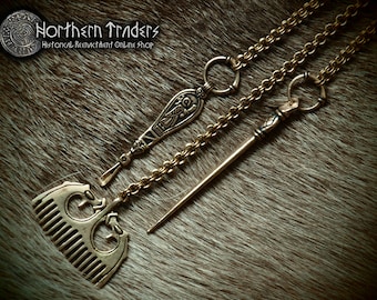 May include: Three antique bronze Viking-style jewelry pieces: a comb pendant, a pendant with an engraved bird design, and a long pin. The pieces are connected by chain and rest on a brown fur-like surface. The image includes the text "Northern Traders Historical Reenactment Online Shop."