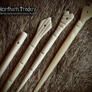 Op de afbeelding: Vier gebroken witte, gladde, langwerpige, naaldachtige instrumenten met kleine gaatjes nabij de top. Elk stuk heeft verschillende uitgesneden kopvormen, waaronder een eenvoudig afgerond uiteinde, een ruit, een hart en een schoppenvorm.