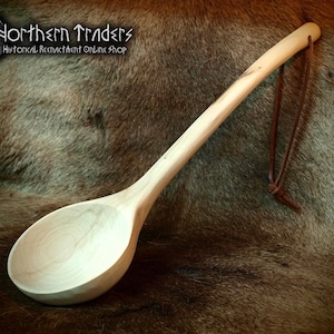 Könnte beinhalten: Handgefertigter Holzlöffel mit langem Stiel und tiefem Löffel. Der Löffel ist aus hellem Holz gefertigt und hat einen Lederriemen am Griff. Der Löffel ist etwa 30 cm lang.