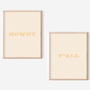 May include: Two framed prints with a light beige background and yellow text. The first print says "HOWDY" and the second print says "Y'ALL".