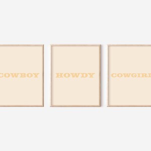 May include: Three framed prints with a light beige background and a light orange text. The prints read "COWBOY", "HOWDY", and "COWGIRL".