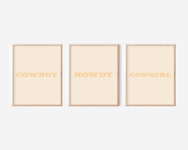 May include: Three framed prints with a light beige background and a light orange text. The prints read "COWBOY", "HOWDY", and "COWGIRL".