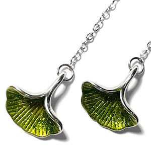 May include: A pair of silver earrings featuring a ginkgo leaf design. The leaves are a vibrant green with a textured appearance, and the earrings hang from delicate silver chains. The background is plain white.