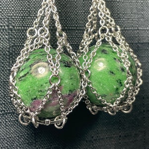 Puede incluir: Un par de pendientes de cadena plateada con esferas de piedras preciosas verdes y rosas colgando.
