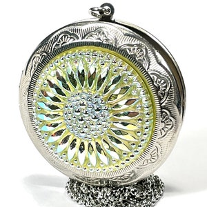 May include: A silver locket with a sunflower design on the front. The locket has a chain attached to it.