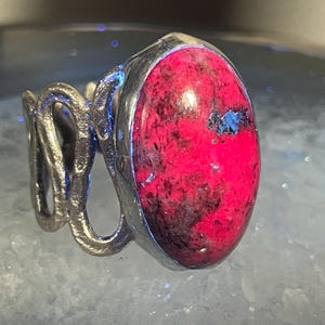 May include: A silver ring with a large, oval-shaped, pink and black gemstone set in the center.