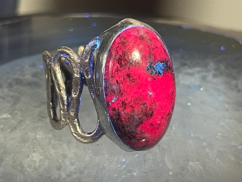 May include: A silver ring with a large, oval-shaped, pink and black gemstone set in the center.