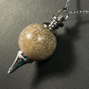 May include: A silver chain with a brown and white stone pendulum. The pendulum is round and has a pointed tip.
