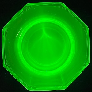 May include: A bright green, octagonal glass dish with a smooth, rounded interior. The dish is made of uranium glass, which glows under a black light.
