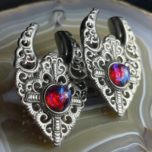 May include: A pair of silver ear gauges with intricate filigree designs and red opal gemstones.