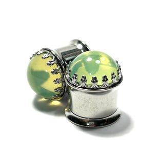 May include: A pair of green glass ear gauges with a silver crown design. The gauges are made of surgical steel and are available in a variety of sizes.