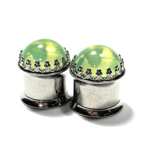 May include: A pair of silver ear gauges with a green glass insert and a decorative crown-like border.