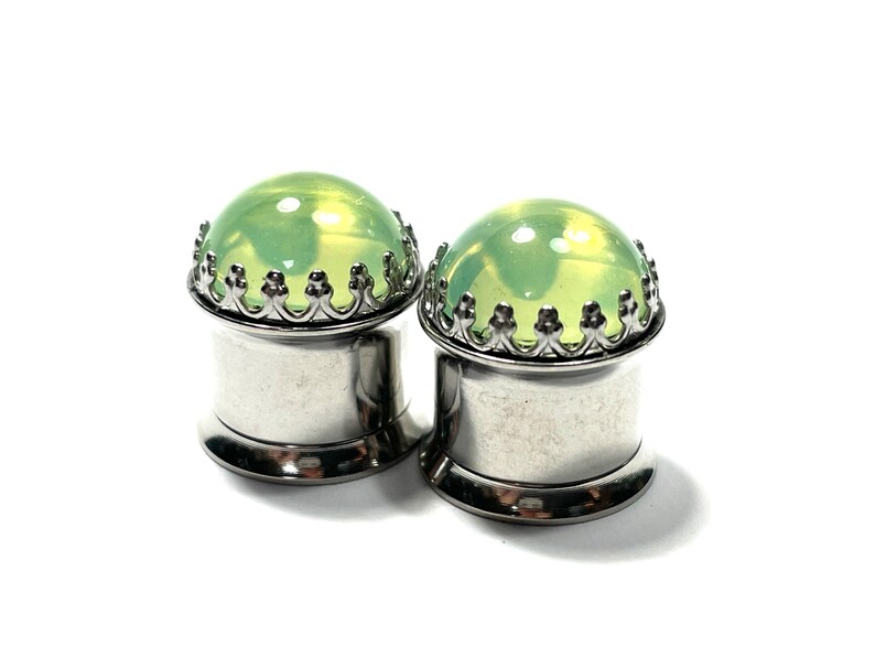May include: A pair of silver ear gauges with a green glass insert and a decorative crown-like border.