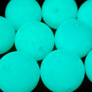 Puede incluir: Primer plano de varias esferas brillantes de color turquesa. Las esferas tienen una superficie ligeramente texturizada y están dispuestas juntas sobre un fondo oscuro. Parecen emitir una luz suave e interna.