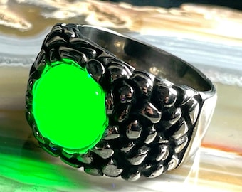 May include: A silver-toned metal ring featuring a textured, scale-like band design surrounding a large, circular, vibrant neon green center stone. The metallic surface of the ring has a polished finish that reflects light across its uneven, bumpy surface.