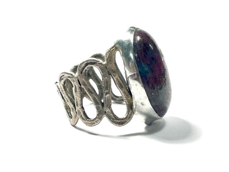 May include: A silver ring with a large, oval-shaped, dark red gemstone set in a silver bezel. The band of the ring is made of twisted silver.