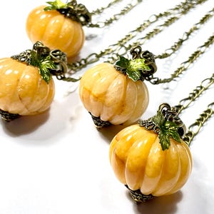 May include: Four pumpkin-shaped pendants on chains. The pumpkins are a light orange color with vertical ridges. Each pumpkin has a decorative metal cap with green leaves. The chains are a bronze color.